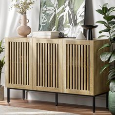 a sideboard with wooden slats on it in front of a painting and potted plants