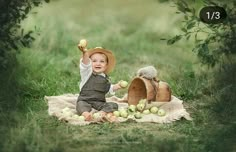 a baby sitting on a blanket with apples in front of him and an apple basket