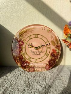 a pink clock sitting on top of a table next to flowers