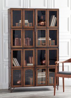 a wooden chair sitting next to a tall book case filled with books and other items