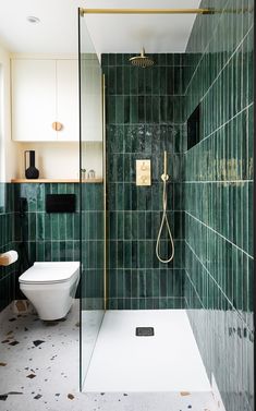 a green tiled bathroom with a white toilet and shower head in the corner, along with black tiles on the walls