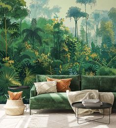 a green couch sitting in front of a forest wall mural