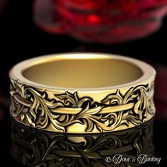 a gold wedding band with an intricate design on the outside and inside, sitting in front of a red glass bowl