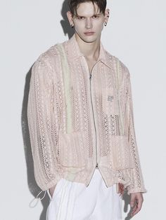 a male model in a light pink jacket and white pants with his hands on his hips