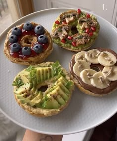 four pastries are arranged on a white platter with blueberries, bananas and kiwi