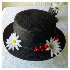 a black hat with white daisies and cherries on it sitting on a table