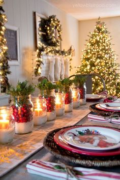 a table topped with lots of glass jars filled with lit candles next to a christmas tree