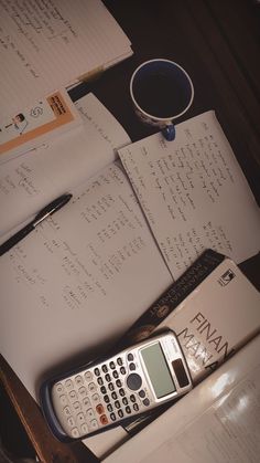 a calculator, notebooks and pen are on a desk with paper work