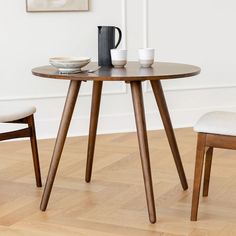 a wooden table with two chairs and a coffee mug on top of it in front of a white wall