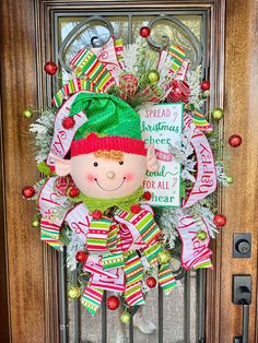 a christmas wreath on the front door with a elf doll hanging from it's side