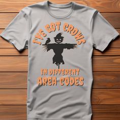 "Introducing our hilarious and quirky Halloween t-shirt that's sure to turn heads and elicit a good laugh! Prepare to sow some laughter this spooky season with our \"I've got crows in different area codes\" t-shirt, featuring an adorably mischievous scarecrow front and center. Crafted from premium, soft cotton, our t-shirt guarantees a comfortable fit that'll keep you at ease whether you're trick-or-treating, attending a costume party, or just enjoying the spooky vibes. The fabric ensures breathability and durability, making it perfect for all your Halloween adventures. Get ready to spread the joy - order yours today and get set to sow some laughter!" Novelty T-shirt With Funny Print For Fall, Funny Halloween T-shirt With Text Print, Funny Halloween Text Print T-shirt, Halloween Short Sleeve T-shirt With Text Print, Halloween Text Print Short Sleeve T-shirt, Funny Halloween T-shirt With Screen Print, Fun Halloween T-shirt Pre-shrunk, Fun Halloween Pre-shrunk T-shirt, Fun Pre-shrunk Halloween T-shirt