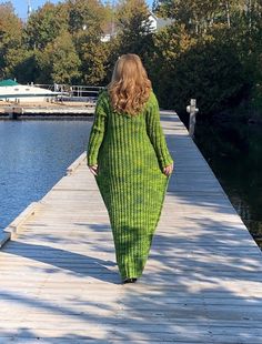 a woman walking on a dock in a green knitted dress with long sleeves and an open back