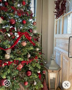 a christmas tree with red and silver ornaments on it next to a lantern in front of a door