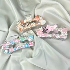 three hair clips with bows and hearts on them sitting on a white satin surface,