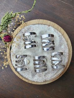 six metal rings sitting on top of a wooden board next to flowers and herbs in the background