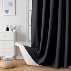 a bath tub sitting next to a window covered in black shower curtaines and rugs