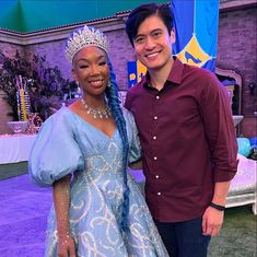 a man standing next to a woman wearing a tiara on top of a purple carpet