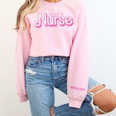 Show your nursing pride with our cozy sweatshirt personalized with your name on the sleeve. This thoughtful design celebrates your dedication to caring for others while adding a touch of feminine charm. Stay warm and stylish during those long shifts, making a statement that's uniquely yours. PRODUCT DETAILS:  unisex sizing  medium-heavy fabric blend of 50% cotton and 50% polyester (heather sport colors - 60% polyester, 40% cotton)  tear-away label  classic fit - runs true to size  colors may differ slightly due to variances in computer screen settings  direct-to-garment printing is used which means the design is sunken into the fabric and will most likely not appear as vibrant in reality as you see on the screen CARE INSTRUCTIONS:  machine wash cold or warm (max 30C or 90F)  non-chlorine b Cute Customizable Long Sleeve T-shirt, Customizable Cute Crew Neck Tops, Personalized Pink Crew Neck Sweater, Pink Long Sleeve Sweatshirt With Name Print, Pink Long Sleeve T-shirt With Name Print, Customizable Cute Long Sleeve Top, Cute Customizable Long Sleeve Top, Personalized Cute Crew Neck Sweater, Personalized Pink Long Sleeve Sweater