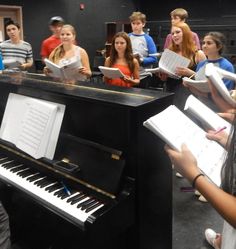 a group of young people standing around a piano