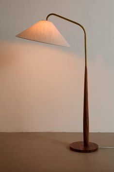 a wooden table lamp with a white shade on the top and bottom, in front of a beige wall