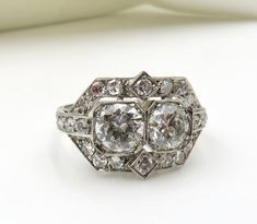 "Circa 1950's. Double Happiness: Stunning geometric, platinum setting featuring 2 round brilliant cut diamonds, each bead set into an octagonal shaped setting which pairs them so beautifully. The accent diamonds within a diamond shape, at the top and bottom also adds to the geometric balance of this sparkling ring. A beautiful symbol of \"two together\" a perfect ring for an engagement or anniversary. And of course, a beautiful ring for a collection. The two (2) central diamonds are a total of 1 Art Deco Octagon Diamond Ring In Diamond White, Art Deco Diamond White Octagon Diamond Ring, Art Deco Octagon Diamond White Ring, Silver Art Deco Diamond Ring With Octagon Shape, Vintage Octagon Diamond Jewelry, Silver Octagon Art Deco Diamond Ring, Formal Octagon Diamond Ring With Accents, Octagon Platinum Diamond Ring With Single Cut Diamonds, Formal Octagon Platinum Diamond Ring