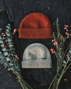 two knitted hats sitting next to each other on top of a wooden table surrounded by greenery