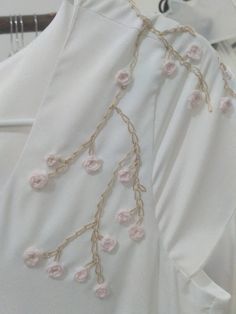 a white dress with pink flowers on it and some gold chains hanging from the back