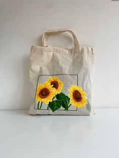 a tote bag with sunflowers painted on the front and side, sitting on a white surface