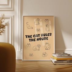 a cat rules the house poster in front of a stack of books on a wooden floor