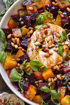 a white bowl filled with chicken, beets and spinach on top of a wooden table