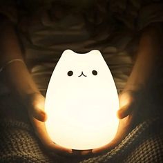 a person holding a small light in their hands with a cat face drawn on it