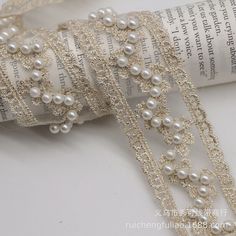 a roll of white ribbon with pearls on it next to a roll of book pages