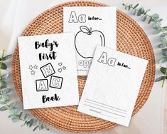 three baby's first books are sitting on a wicker plate next to eucalyptus leaves