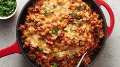 a skillet filled with ground beef and cheese next to a small bowl of greens