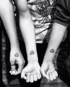 two people are holding hands with tattoos on their arms and one is holding the other's hand