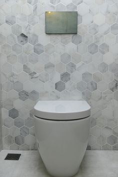 a white toilet sitting inside of a bathroom next to a tiled wall covered in hexagonal tiles