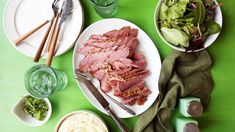 a green table topped with white plates filled with meat and veggies next to salad