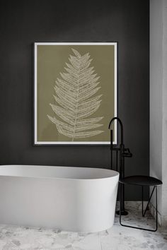 a white bath tub sitting next to a black chair in a bathroom under a framed leaf print