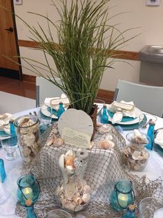 a table set up with plates, cups and vases for an ocean themed dinner