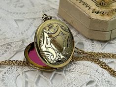 "Description: An antique etched round gold plated locket on a 14K gold filled chain. The front of this pendant features an etched central heart that is surrounded with ornate lines in a geometric type of design with angled sides around the remainder of the front. There are small etched flowers at the top and the bottom of the central heart shape. The back of this locket is plain with no design and has a shiny finish. The sides of the round locket are somewhat flat, not rounded as most lockets ar Gold Etched Locket Necklace For Keepsake, Gold Locket Necklace With Intricate Round Pendant, Gold Locket Necklace With Intricate Design And Round Pendant, Gold Locket Necklace With Intricate Design, Ornate Gold Round Locket Necklace, Elegant Gold Etched Locket Necklace, Gold Filigree Medallion Locket Necklace, Gold Medallion Locket Necklace With Filigree, Heirloom Brass Locket Necklace Hallmarked