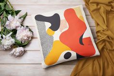 a pillow with an abstract painting on it next to flowers