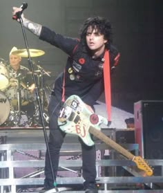 a man with black hair holding a guitar on stage