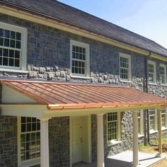 a stone building with white pillars and windows on the front, covered by a metal roof