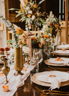 the table is set with gold and white plates, silverware, flowers and candles