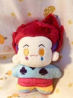 a small stuffed toy with red hair and eyes sitting on top of a white sheet