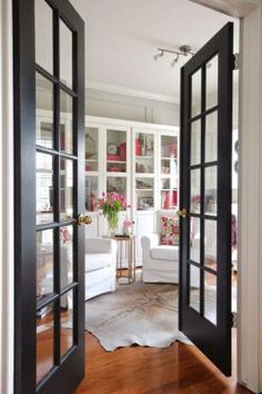 an open door leading into a living room with white furniture and flowers in vases