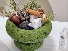 a green bowl filled with rocks and plants next to a bottle of water on a table