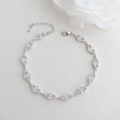 a white flower sitting on top of a table next to a silver bracelet with crystal stones