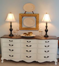 a white dresser with two lamps and plates on top