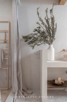 a plant in a white vase sitting on top of a table next to a shower curtain